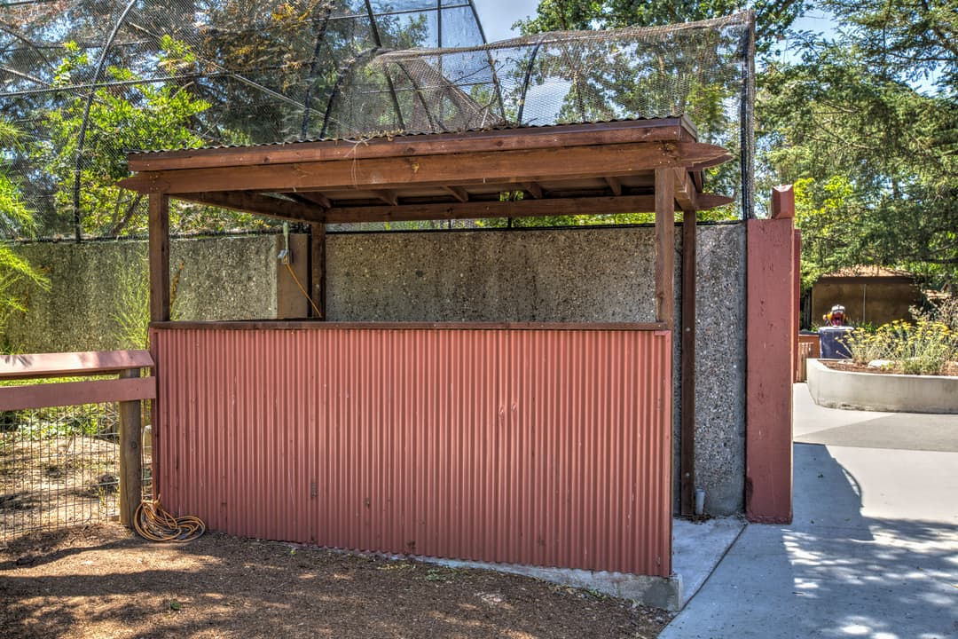 Empty animal enclosure at a zoo with red corrugated metal panels on a sunny day