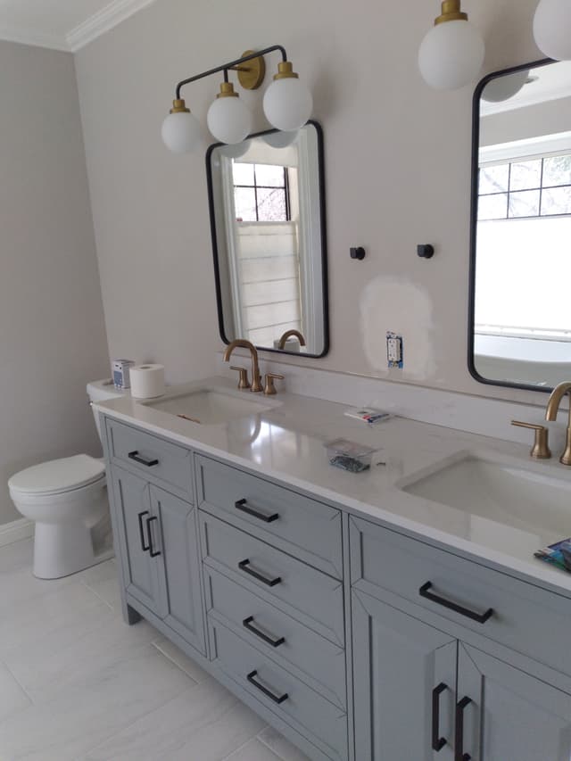 Modern bathroom with double sink vanity, gold faucets, mirrors, and white countertop