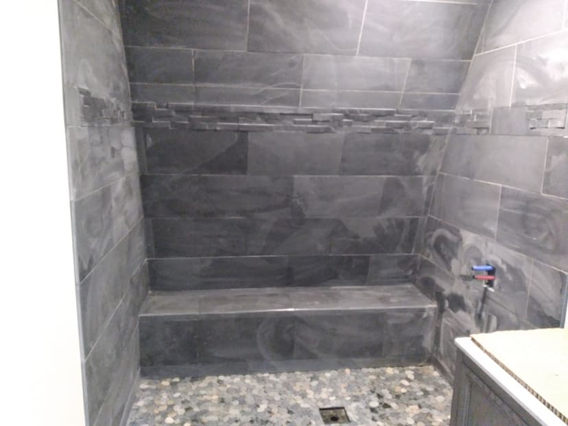Modern shower with black tiles, built-in bench, and pebble floor