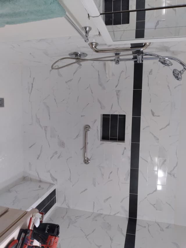 Modern marble-tile shower with bench, grab bar, dual shower heads, and black accent strip