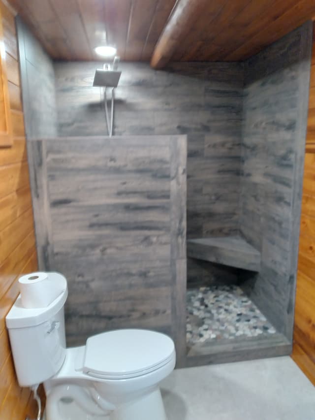 Modern rustic bathroom with wood shower, stone floor, and white toilet