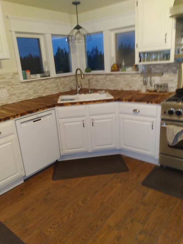 Modern white kitchen with wood countertop, corner sink, and tile backsplash