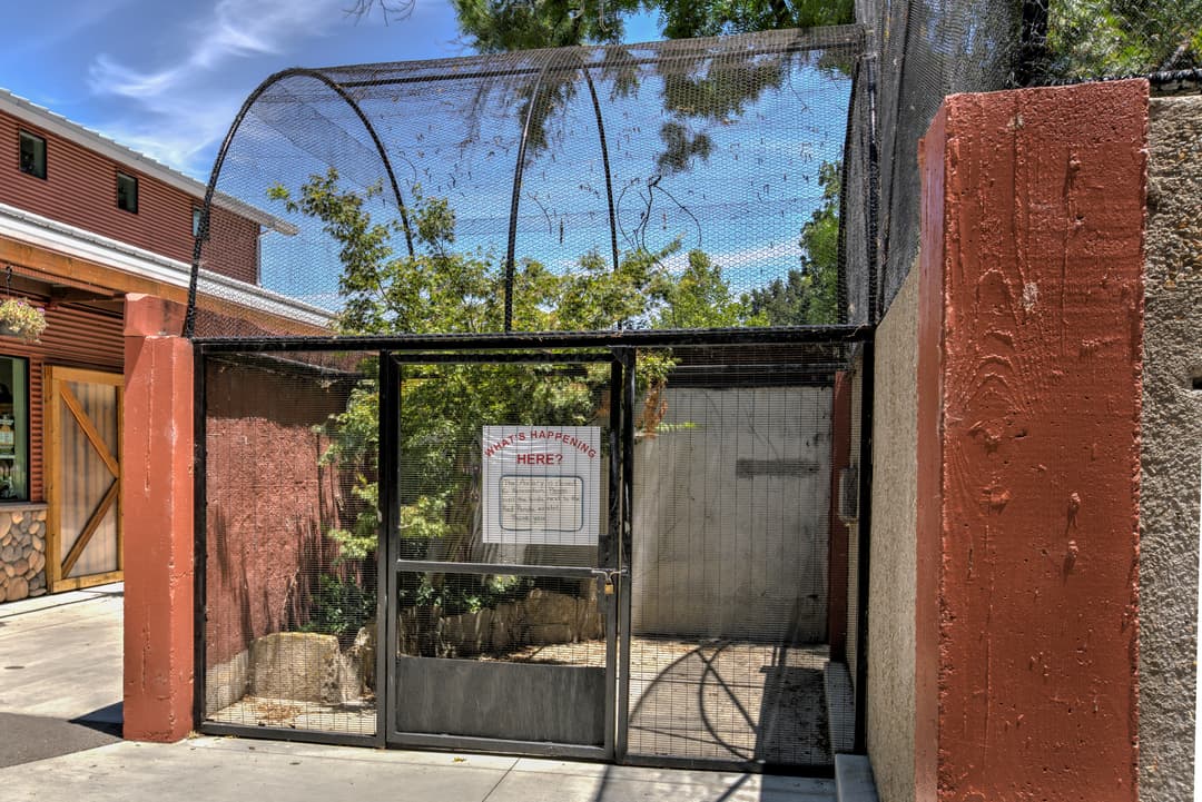 Empty animal enclosure at zoo with sign and mesh fencing